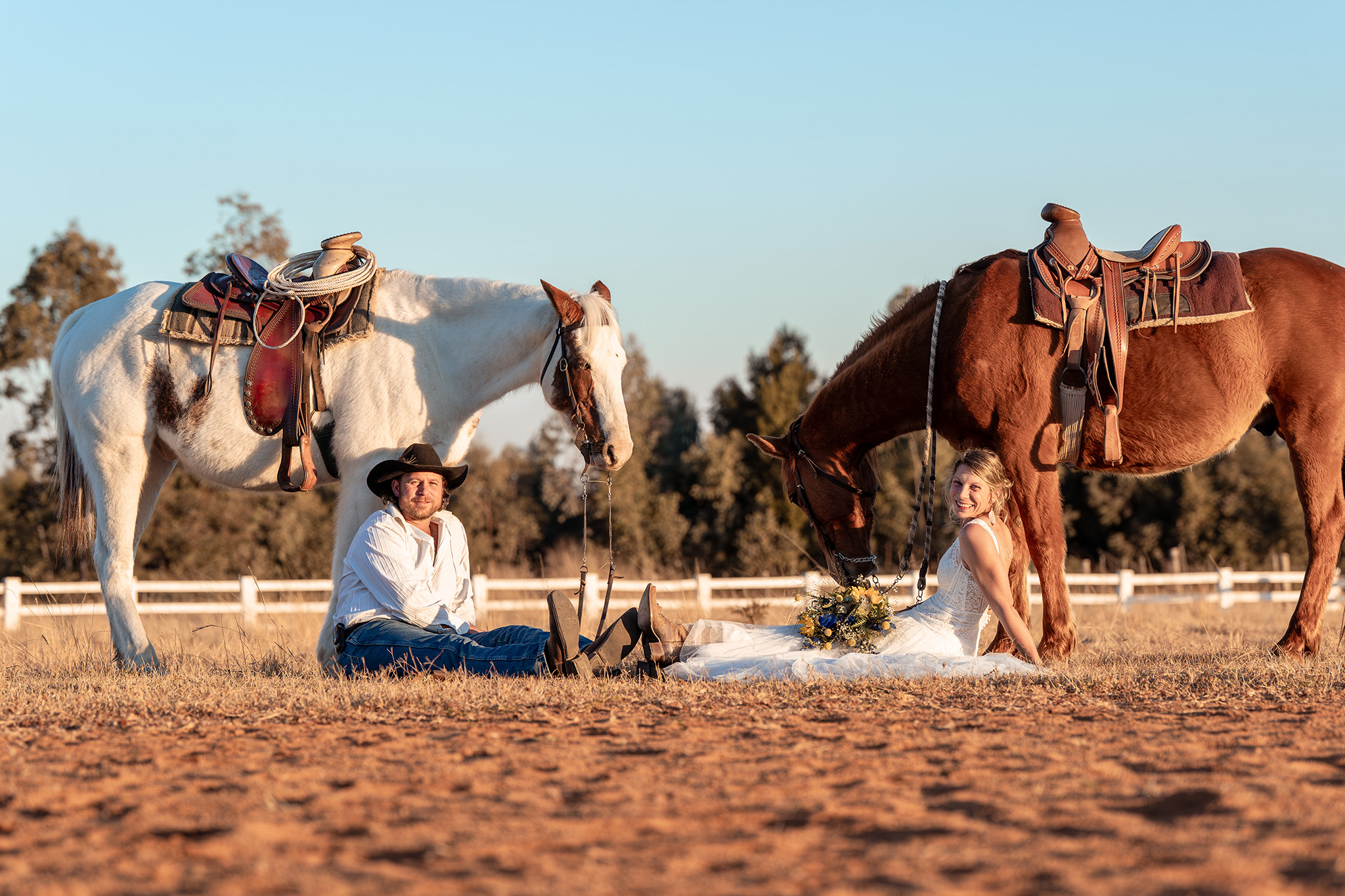 Birde and groom sitting on the ground with their horses