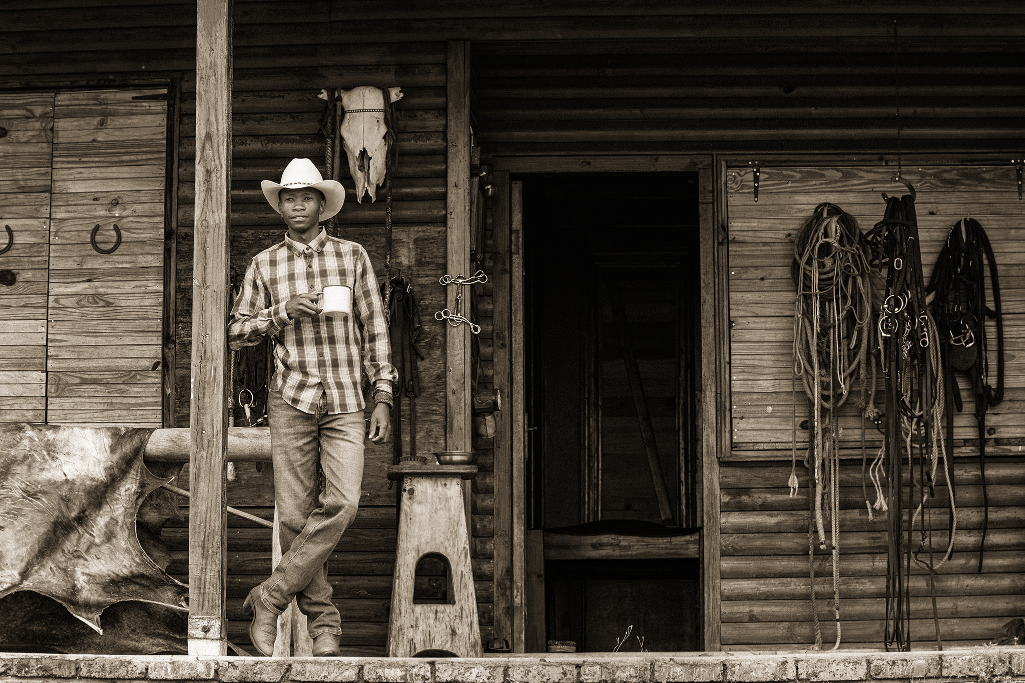 Sepia image of a cowbou in front of a cabin with a cup of coffee