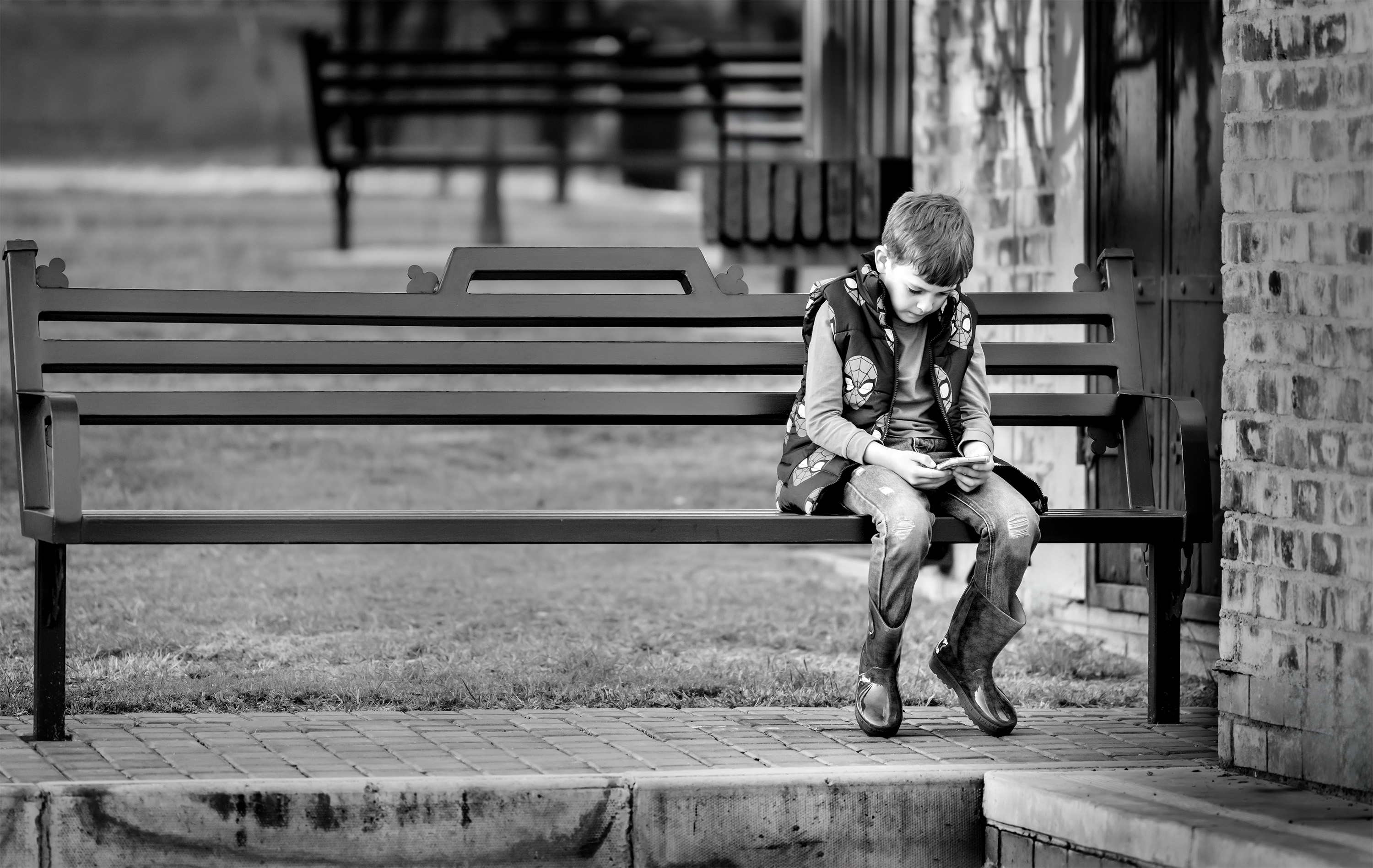 Black and white image of a boy on a bench looking at a phone