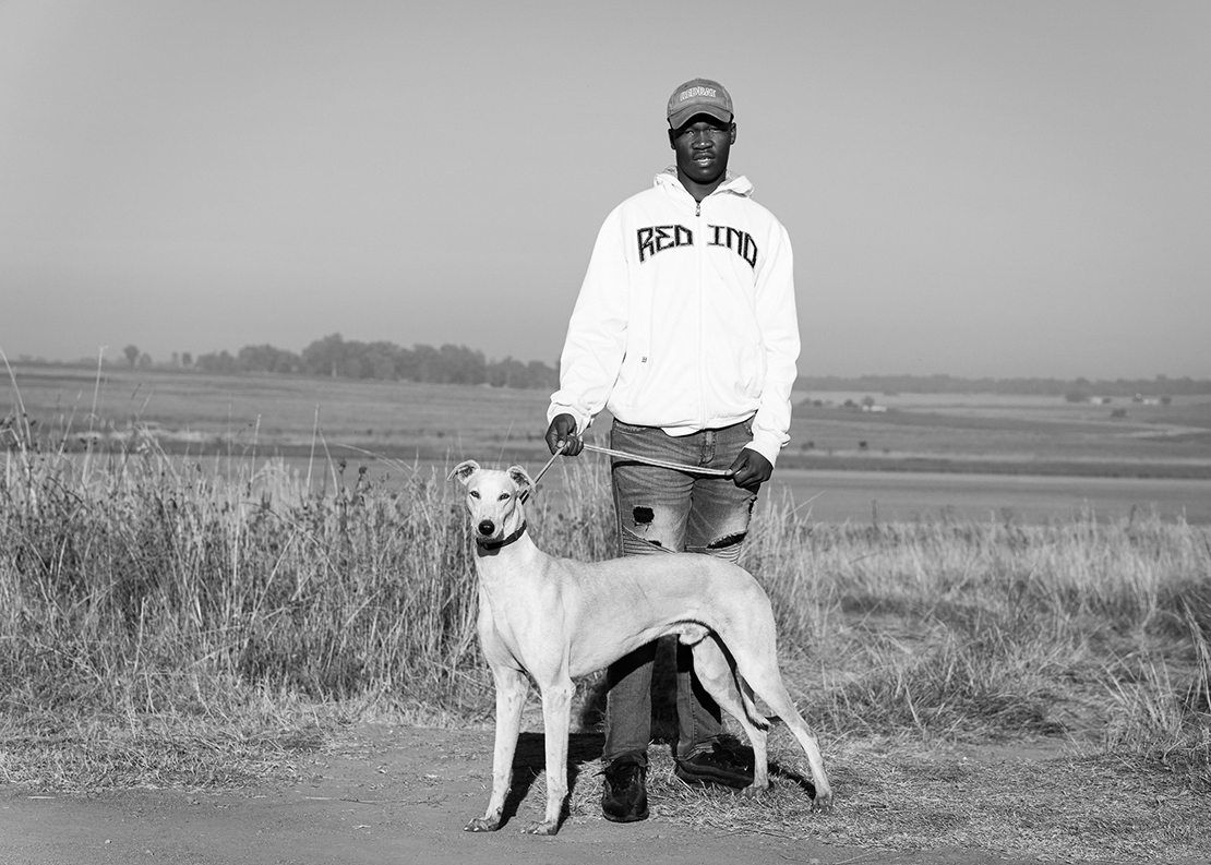 Black and white portrait of a young man with a greyhound