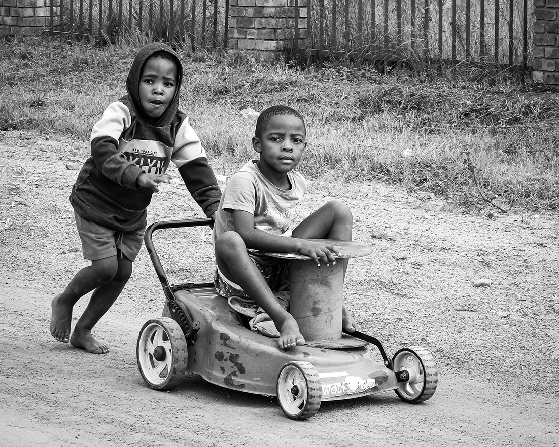 Black and white image of boys playing with a lawnmower in the street